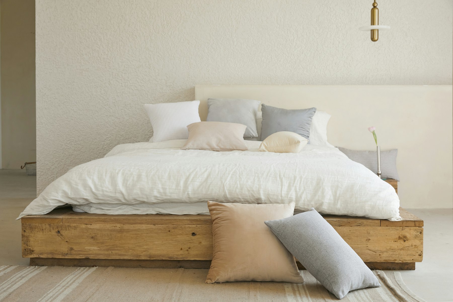 Low oak bed dressed in ivory linen, with pillows and a side table.